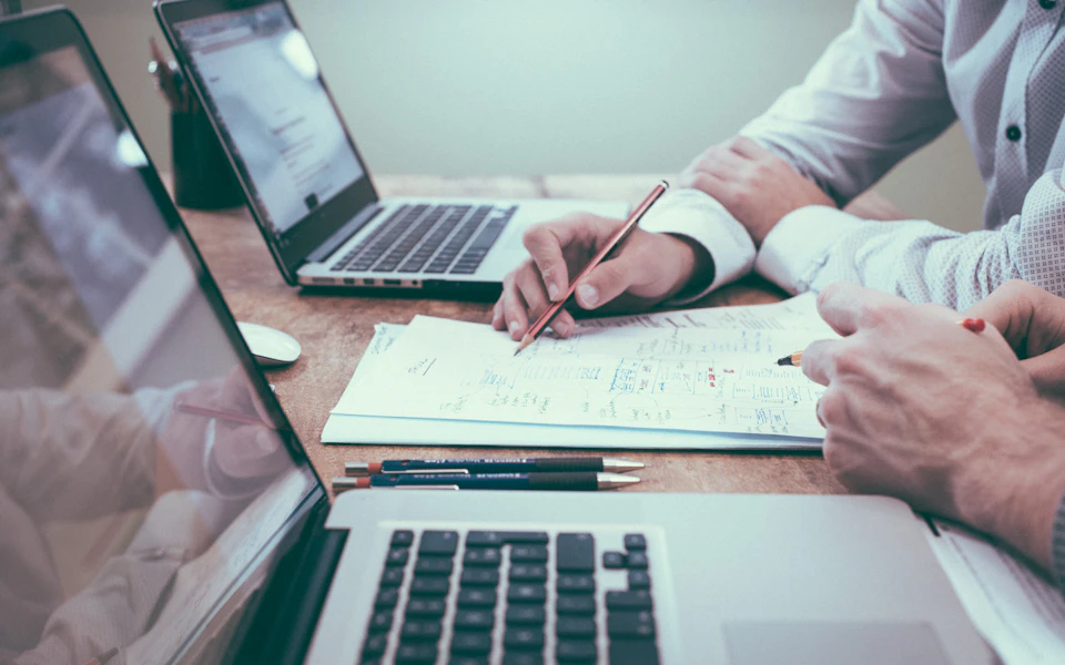 Hands reviewing a business plan beside laptops